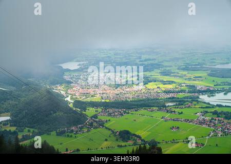 Allemagne, paysage aérien atmosphérique de Füssen avec nuages brumeux et cimes d'arbres ensoleillées de Tegelberg Banque D'Images