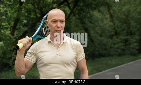 Portrait d'un joueur de tennis mature confiant avec raquette debout à l'extérieur près d'un court de sport. Mode de vie sain, entraînement actif et sport professionnel Banque D'Images