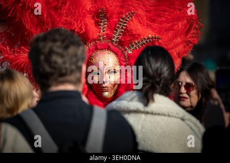 Les fêtards du carnaval se rassemblent autour d'une femme portant un masque rouge et or orné pendant le Carnaval de Venise à Venise, en Italie, mars 2025. Banque D'Images