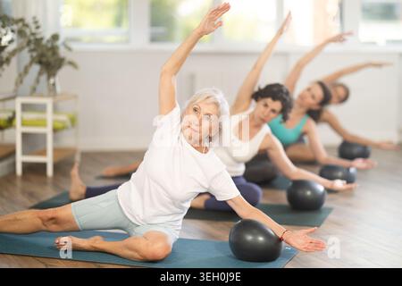 Femme âgée faisant Mermaid Stretch avec Ball dans le studio Pilates du groupe Banque D'Images
