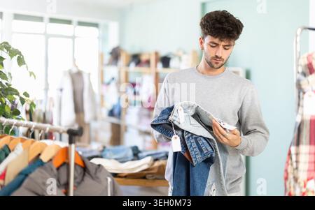 Jeune homme examinant une paire de jeans dans un magasin de vêtements Banque D'Images