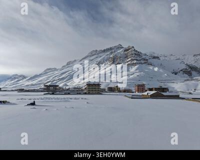 Kaza, Inde - 28 janvier 2026 : vue sur la vallée de Spiti avec des bâtiments enneigés et de majestueux sommets himalayens sous un ciel nuageux hivernal. Banque D'Images