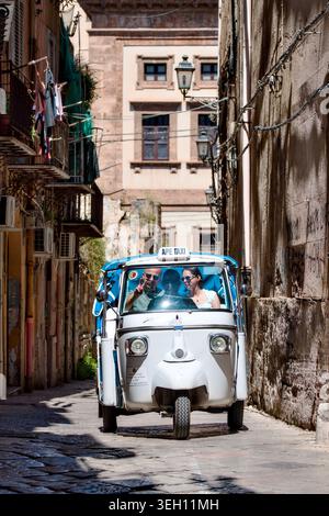 Taxi traditionnel Piaggio APE avec des passagers joyeux conduisant à travers une étroite ruelle historique à Palerme, Sicile, Italie. Banque D'Images