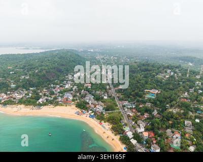 Vue aérienne de la plage d'Unawatuna avec de l'eau turquoise et des bâtiments côtiers nichés au milieu d'une végétation tropicale luxuriante à Unawatuna, Province du Sud, Sri la Banque D'Images