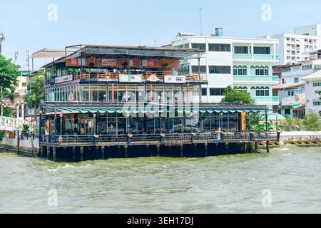 BANGKOK, THAÏLANDE - 27 février 2025 : Café au bord de la rivière sur pilotis au-dessus de la rivière Chao Phraya à Bangkok avec de grandes fenêtres en verre et une terrasse ouverte. Banque D'Images