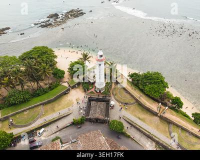 Vue aérienne du phare historique de Galle et des fortifications en pierre du fort de Galle avec des gens sur la plage et des palmiers à Galle, province du Sud Banque D'Images