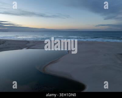 Vue aérienne de Lagoa de Obidos rencontrant l'océan Atlantique à travers une large plage de sable sous un ciel crépusculaire doux à Foz do Arelho, Leiria District, Portu Banque D'Images