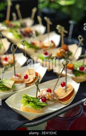 Une variété élégante de mini canapés servis dans des plats blancs élégants en forme de bateau, recouverts d'avocat frais, de crevettes, de fromage à la crème, de laitue et de Be rouge vif Banque D'Images