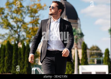 Bel homme en costume et lunettes de soleil marchant dans la ville Banque D'Images