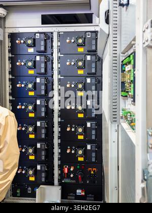 Vue verticale des modules de stockage de batteries au lithium professionnels empilés dans une armoire industrielle, avec ventilateurs de refroidissement et connexions électriques. Banque D'Images