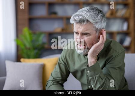 Homme mûr touchant son oreille avec une expression angoissée, souffrant d'un problème de santé tel qu'une perte auditive, une surdité, des douleurs auriculaires ou des acouphènes, éprouvant de l'inconfort et de la difficulté à entendre Banque D'Images