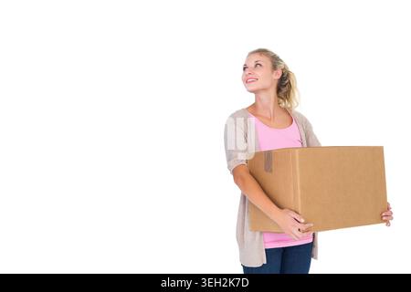 Femme portant un haut rose et un cardigan beige tenant une boîte scellée, regardant vers le haut à gauche dans le studio, espace de copie Banque D'Images