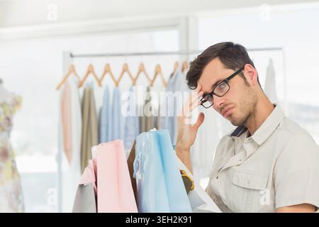 Homme portant des lunettes, chemise beige, tenant des sacs à provisions pastel dans la boutique près du rack, espace de copie Banque D'Images