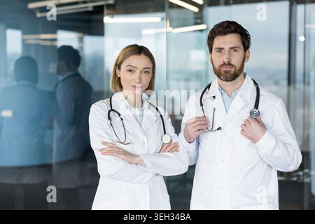 Des professionnels de la santé, un médecin masculin et un médecin féminin, debout côte à côte portant des blouses de laboratoire blanches et des stéthoscopes, représentant les soins de santé et l'expertise dans un environnement clinique moderne Banque D'Images