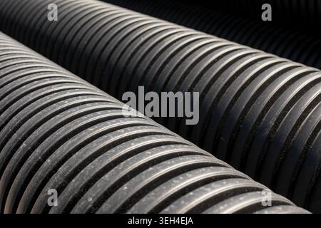 Vue en grand angle de plusieurs tuyaux de drainage en plastique ondulé noir empilés ensemble sur un chantier de construction. Banque D'Images