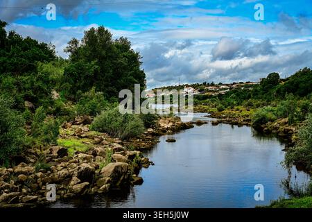 Une rivière tranquille serpente à travers des berges rocheuses et une végétation luxuriante sous des nuages spectaculaires dans le nord du Portugal. Banque D'Images