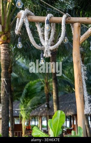 Décor tropical rustique avec ampoules vintage suspendues et détails de corde entourés de palmiers au Vietnam. Banque D'Images