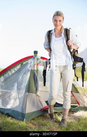 Randonneur féminin debout devant une tente grise verte tenant sac à dos avec tapis roulé sur l'herbe Banque D'Images