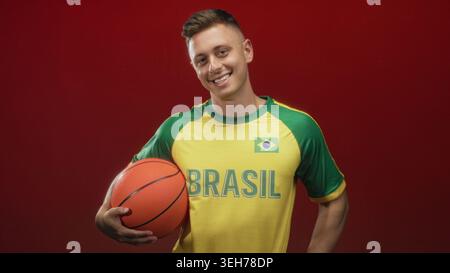 L'homme tient le basket-ball et fait des gestes de main de coeur en studio, portant le maillot brésilien ; fierté de l'esprit d'équipe. Banque D'Images