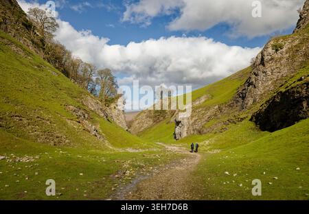 Une paire de marcheurs sur un chemin dans une vallée montagneuse étroite herbeuse avec des falaises et des arbres, Cave Dale, Peak District, Derbyshire, Angleterre. Banque D'Images