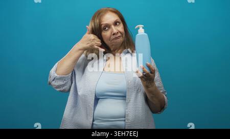 Femme tient une bouteille de savon avec pompe et fait un geste de la main de téléphone dans un studio ; promotion publicitaire d'hygiène ludique. Banque D'Images