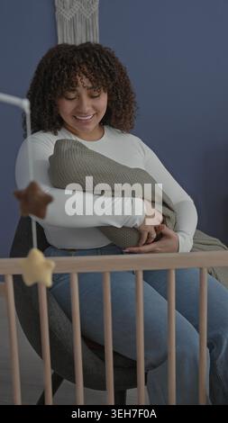 Femme berçant le bébé emmailloté, tapotant à la main la couverture tricotée par le berceau dans le bâtiment de la chambre de bébé, souriant à l'enfant ; tendresse. Banque D'Images