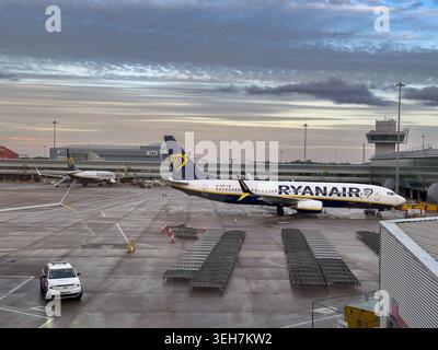Avion de ligne Ryanair garé sur le tarmac de l'aéroport de Manchester, Royaume-Uni, au crépuscule sous un ciel nuageux avec la tour de contrôle en arrière-plan. Banque D'Images