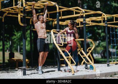 Formation de couple de forme sur l'équipement de calisthenics en plein air jaune dans une séance d'entraînement de parc ensoleillé Banque D'Images
