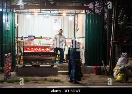 Sri Lanka - 14 janvier 2026 : vue nocturne d'un petit étable de volaille en bordure de route avec un homme debout à l'intérieur sous des lumières vives et une femme attendant dehors Banque D'Images