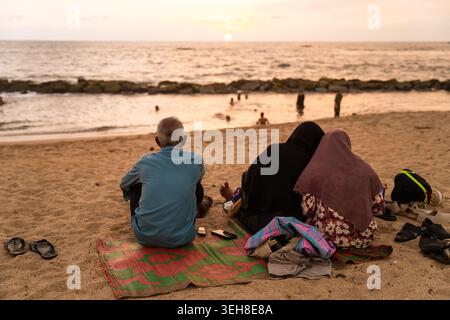 Sri Lanka - 14 janvier 2026 : vue d'un homme et de deux femmes assis sur le sable regardant le coucher de soleil sur l'océan Indien avec de douces vagues et un doux SK Banque D'Images