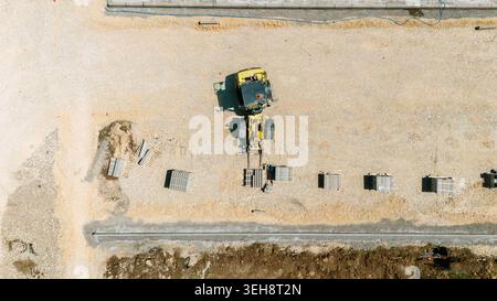 Vue aérienne d'une chargeuse sur pneus jaune déplaçant des matériaux sur un chantier de construction avec des piles de pavés Pancevo, Voïvodine, Serbie. Banque D'Images