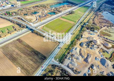Vue aérienne d'un important chantier de construction d'infrastructures avec de nouvelles voies ferrées et des ponts autoroutiers entourés de champs verts et d'étangs près de but Banque D'Images