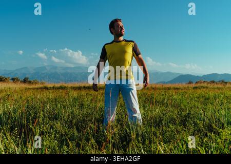Homme debout dans le champ dans le débardeur de sport avec expression heureuse Banque D'Images