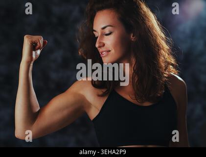 Femme brune en débardeur noir montrant bicep et sourire Banque D'Images