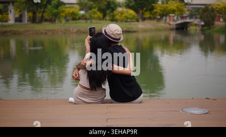 Jeune couple embrassant, prenant une vidéo selfie par le lac tranquille dans un parc Banque D'Images