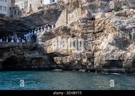 Polignano a Mare, Italie, Pouilles - 24 mai 2024 : bâtiments construits sur des falaises, vue depuis la mer de rochers et grottes de ​​picturesque.terrasse de repos célèbre dans le monde entier Banque D'Images