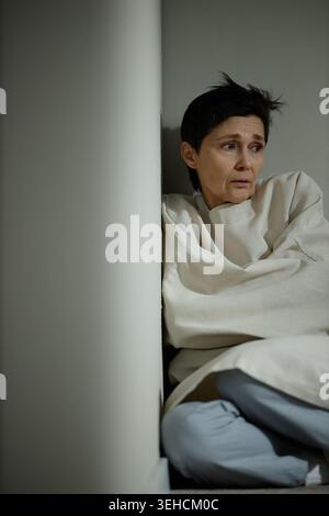 Femme d'âge moyen assise dans un coin exprimant l'anxiété Banque D'Images