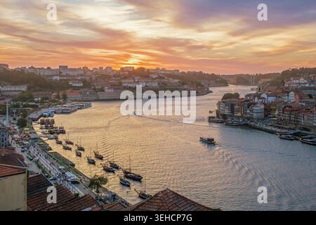 Coucher de soleil sur le fleuve Douro, Ribeira do Porto, Portugal, et Vila Nova de Gaia avec des bateaux rabelo amarrés par le quai et des bateaux touristiques dans la rivière Banque D'Images