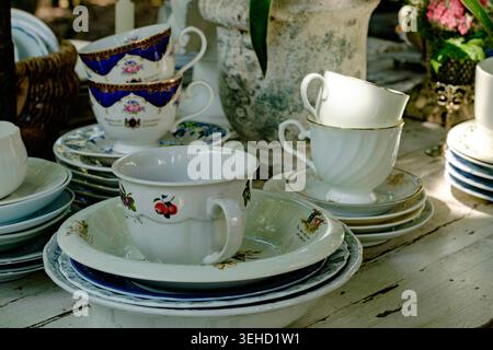 Une collection de belles tasses à thé et soucoupes antiques en porcelaine exposées sur une table rustique dans un marché vintage Banque D'Images