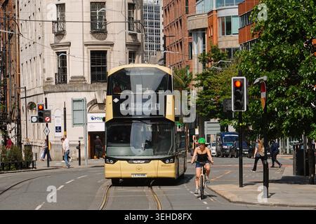 Un bus électrique à impériale jaune et noir Bee Network et une cycliste dans une rue de Manchester City cent Banque D'Images