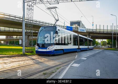 Tramway moderne à plancher surbaissé en livrée bleue et blanche conduisant sur des voies à travers une intersection urbaine près des passages supérieurs en béton pour les transports publics conc Banque D'Images