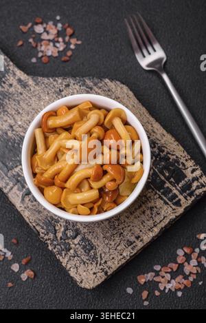 Nourriture, délicieux champignons au miel marinés avec du sel et des épices dans une assiette en céramique sur un fond texturé foncé Banque D'Images