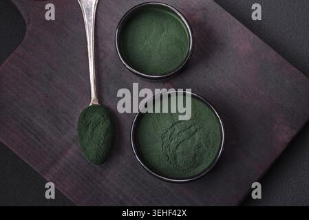 Nourriture, épices, spiruline de couleur verte sous forme de poudre dans un bol noir sur un fond de béton foncé Banque D'Images