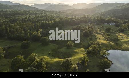 Vue aérienne capture la beauté sereine d'un paysage verdoyant luxuriant baigné dans la lueur chaude du coucher du soleil, avec des montagnes lointaines se fanant dans la brume Banque D'Images
