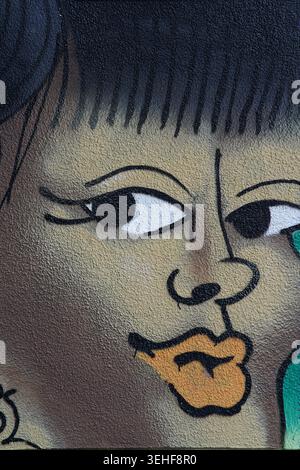 Portrait en gros plan stylisé d'une femme aux lèvres orange frappantes, aux cheveux noirs audacieux et aux yeux expressifs dans une murale de Street art vibrante à Brighton, en Angleterre. Banque D'Images