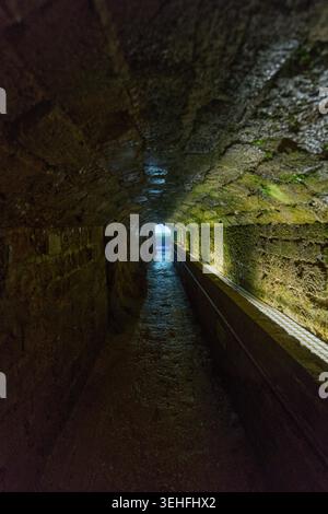 Passage souterrain avec murs de pierre mouillés, mousse, et une sortie lumineuse lointaine. Représenter l'espoir, l'avenir et le changement Banque D'Images