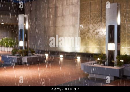 Une forte pluie tombe la nuit dans un cadre architectural urbain. La scène capture des pluies torrentielles avec des traînées verticales de gouttes d'eau Banque D'Images