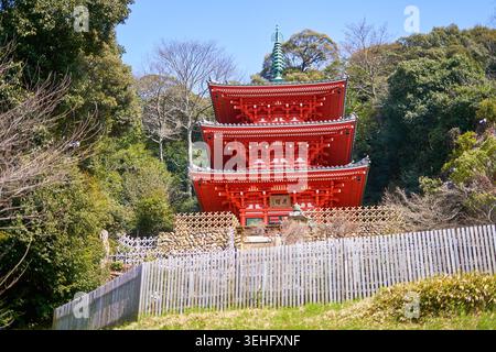 Un pagode japonais traditionnel à trois étages (sanju-no-to) avec une architecture en bois rouge éclatante se dresse de manière proéminente devant un arrière-plan de verdure luxuriante Banque D'Images