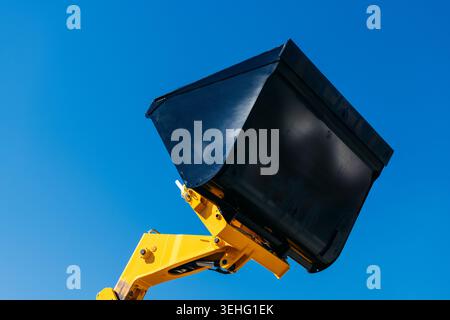Godet de pelle jaune soulevé contre un ciel bleu vif, mettant l'accent sur les machines de construction, l'équipement lourd et la puissance industrielle dans un CLO propre et audacieux Banque D'Images