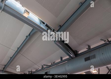 Plafond intérieur contemporain présentant des poutres métalliques apparentes, des conduits incurvés et des panneaux perforés, mettant en valeur le design industriel, la géométrie structurelle Banque D'Images
